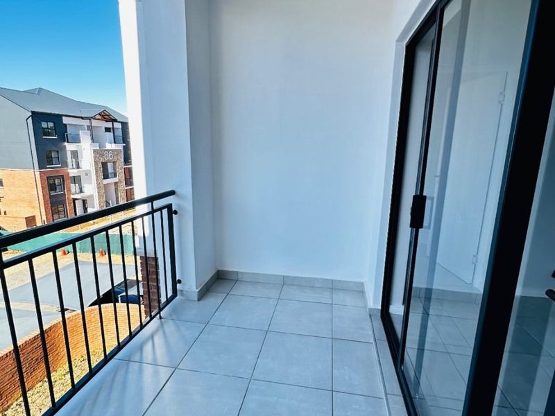 A clean, modern balcony featuring tiled flooring, a secure metal balustrade, and large sliding glass doors providing access to the interior.