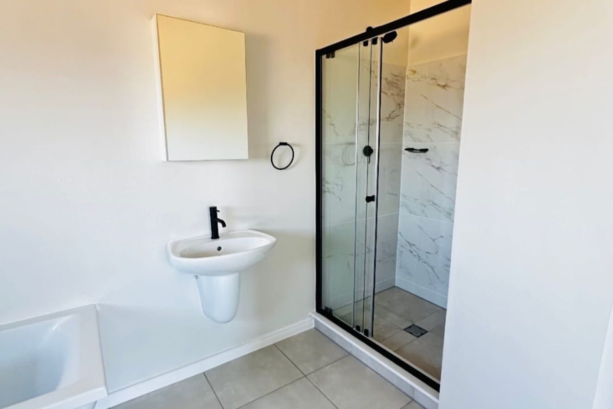 Modern bathroom featuring a wall-mounted basin, black fixtures, and a glass-enclosed shower with marble-look tiling.