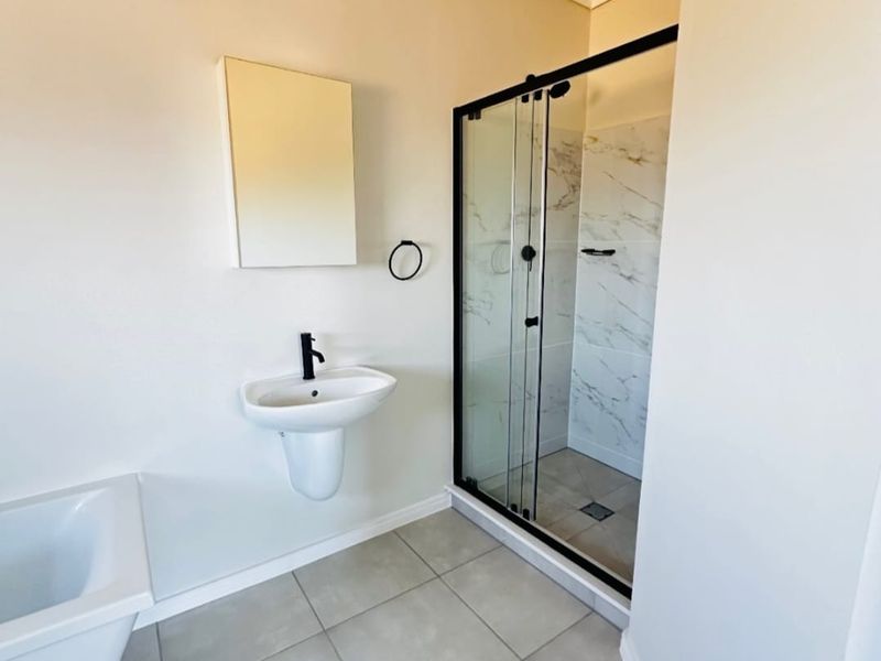 Modern bathroom featuring a wall-mounted basin, black fixtures, and a glass-enclosed shower with marble-look tiling.