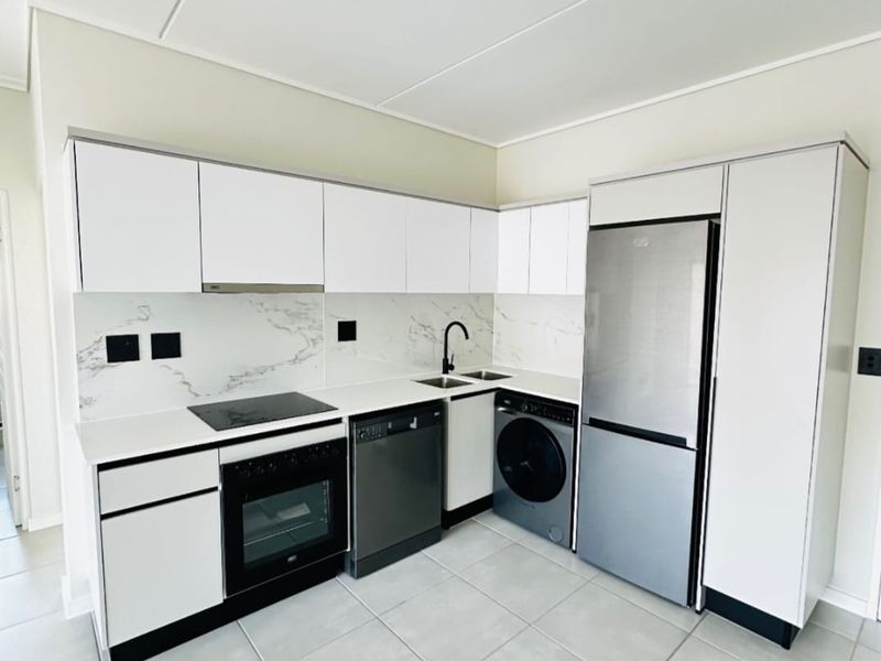 Modern kitchen featuring white cabinetry, marble-look splashback, integrated appliances, and sleek track lighting, finished with neutral floor tiles.