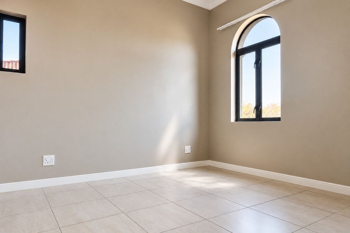 A bright, empty bedroom featuring neutral walls, tiled flooring, and a distinctive arched window, providing a clean canvas for interior design.