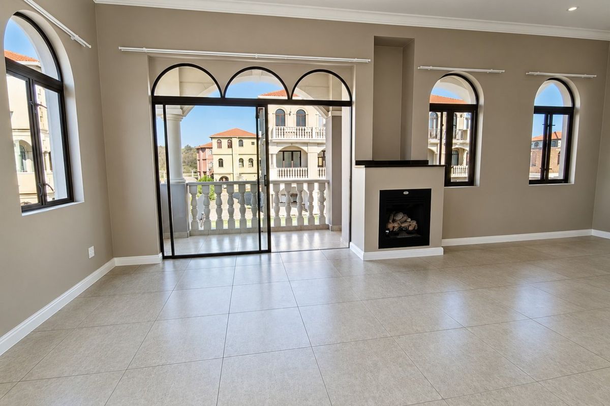 Spacious living room featuring neutral tiled flooring, a built-in fireplace, and large arched windows leading to a private balcony with balustrade detailing.