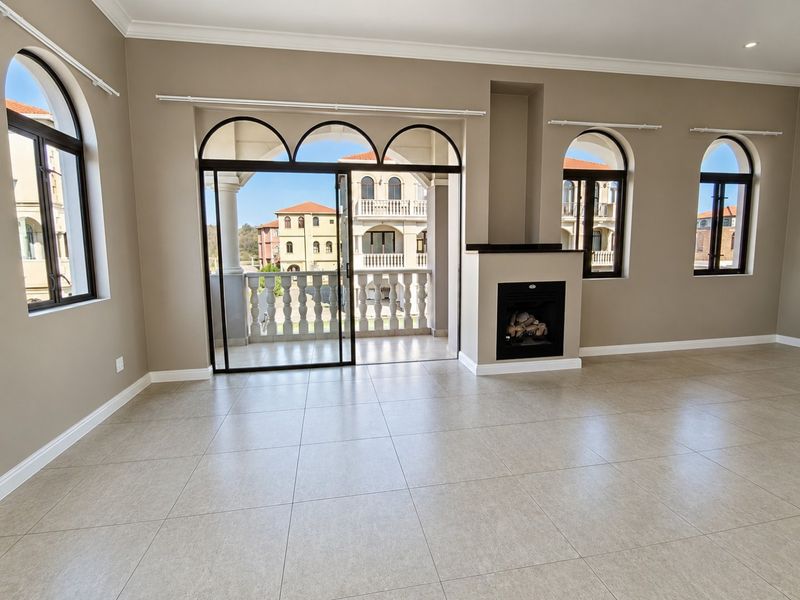 Spacious living room featuring neutral tiled flooring, a built-in fireplace, and large arched windows leading to a private balcony with balustrade detailing.