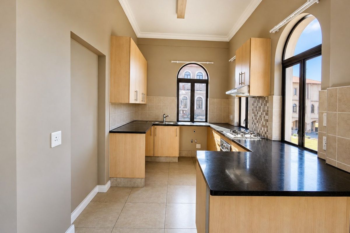 A clean, modern kitchen featuring light wood cabinetry, dark granite countertops, a gas hob, and arched windows providing ample natural light.