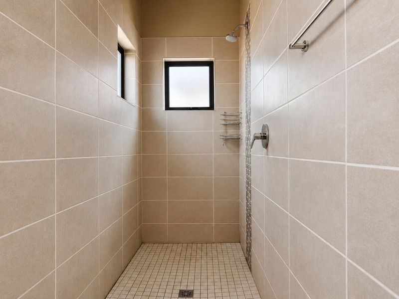A clean, modern walk-in shower featuring neutral wall tiles, a mosaic accent strip, and a frosted window for natural light and privacy.