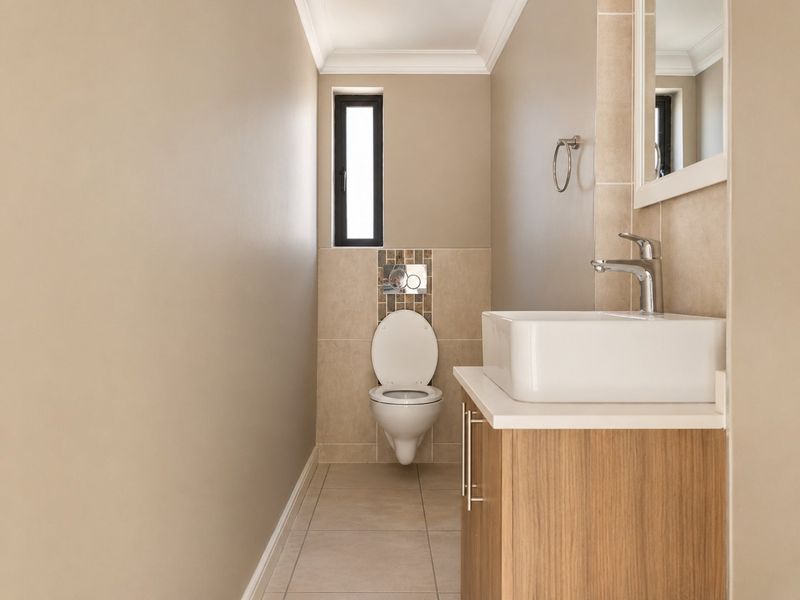 A modern, well-maintained guest bathroom featuring a wall-mounted toilet, a sleek vanity with a vessel sink, and neutral tiled finishes.