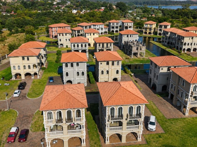 Aerial view of a residential estate featuring multi-story homes with terracotta roofs, arched balconies, and surrounding water canals.
