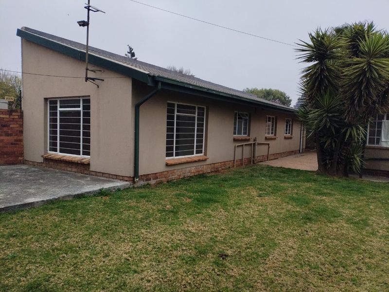 Rear view of the house featuring a tiled roof, steel-framed windows with security bars, and a concrete patio area adjacent to the lawn.