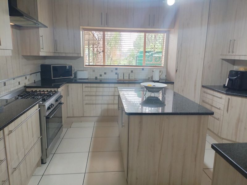 Modern kitchen featuring light wood-finish cabinetry, granite countertops, a central island, and a gas stove with an extractor fan.