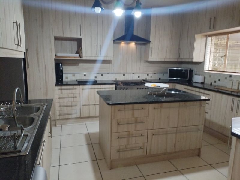 Modern kitchen featuring light wood-grain cabinetry, granite countertops, a central island, and a tiled backsplash with integrated extractor fan.