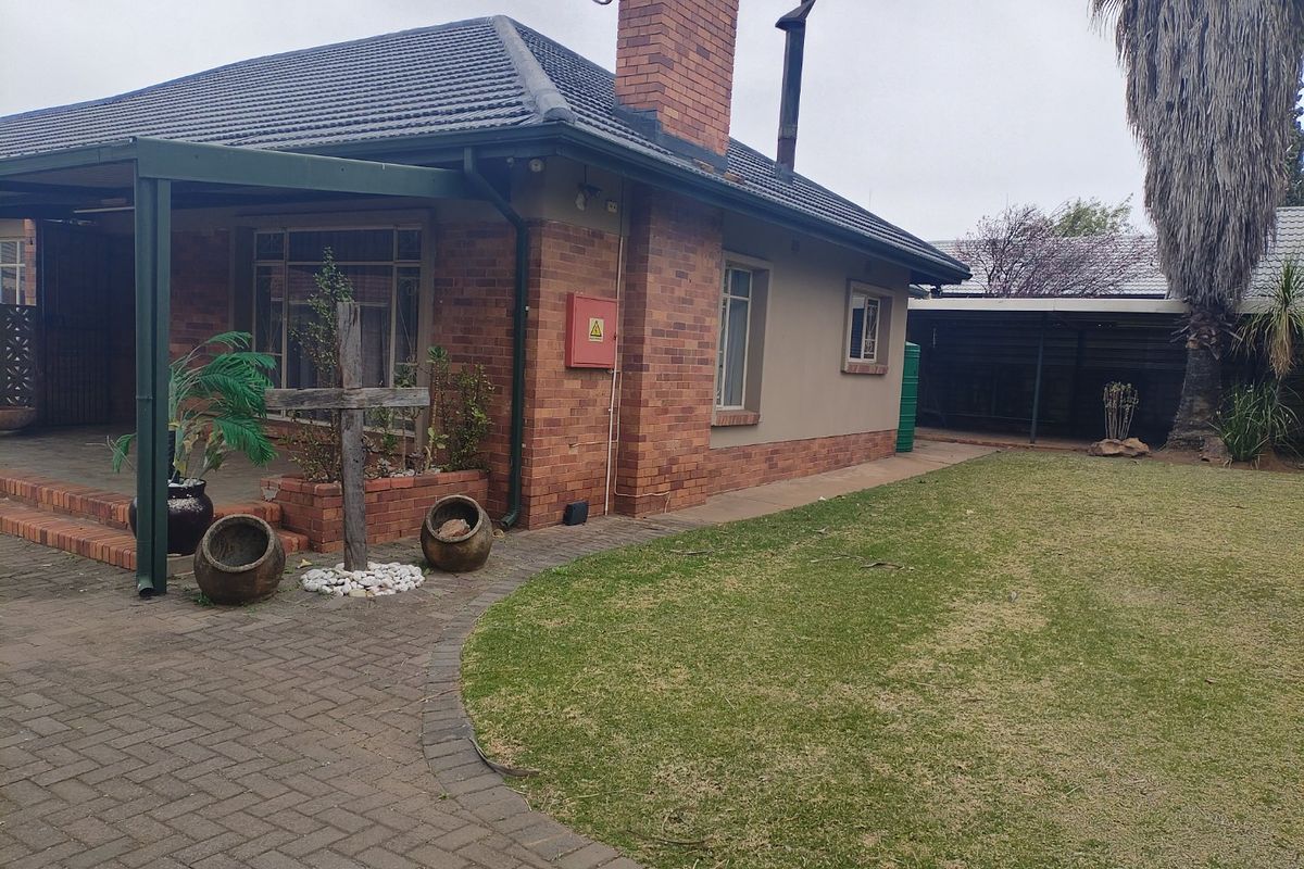 Rear view of a brick house featuring a covered patio area, paved walkway, and a well-maintained lawn.