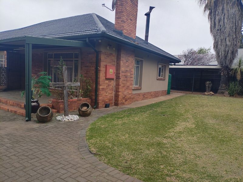 Rear view of a brick house featuring a covered patio area, paved walkway, and a well-maintained lawn.
