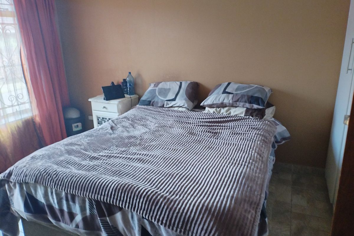 A functional bedroom featuring tiled flooring, a built-in wardrobe, and a window fitted with a security gate.