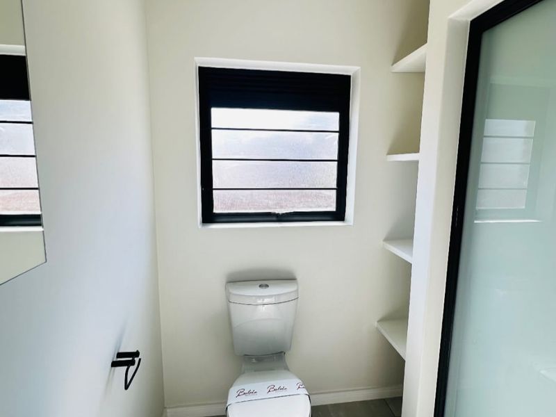 A clean, modern bathroom featuring tiled floors, a white toilet, built-in shelving, and a frosted glass door with black framing.