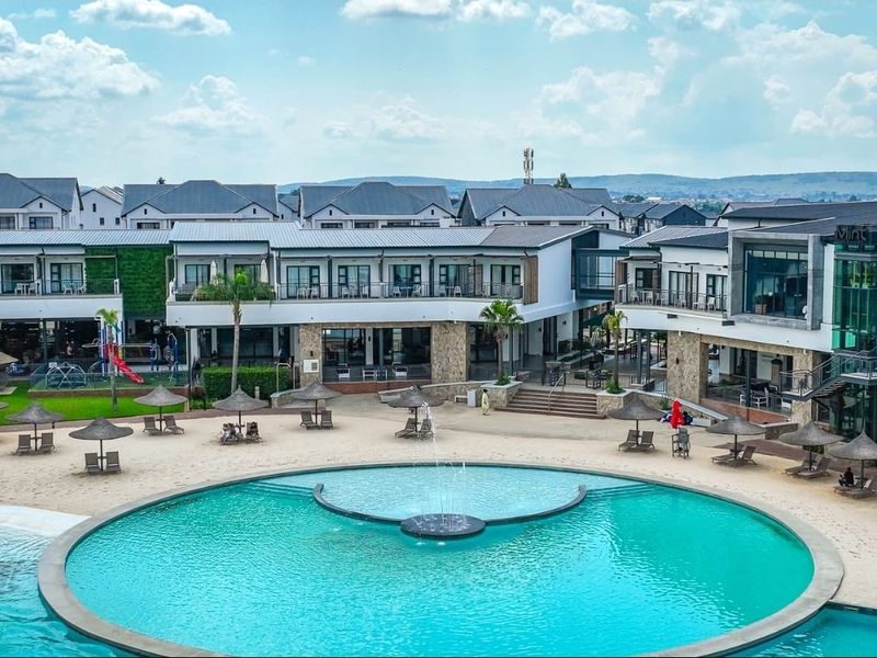 A well-maintained apartment complex featuring a large central swimming pool with a fountain, surrounded by landscaped grounds and modern building facades.