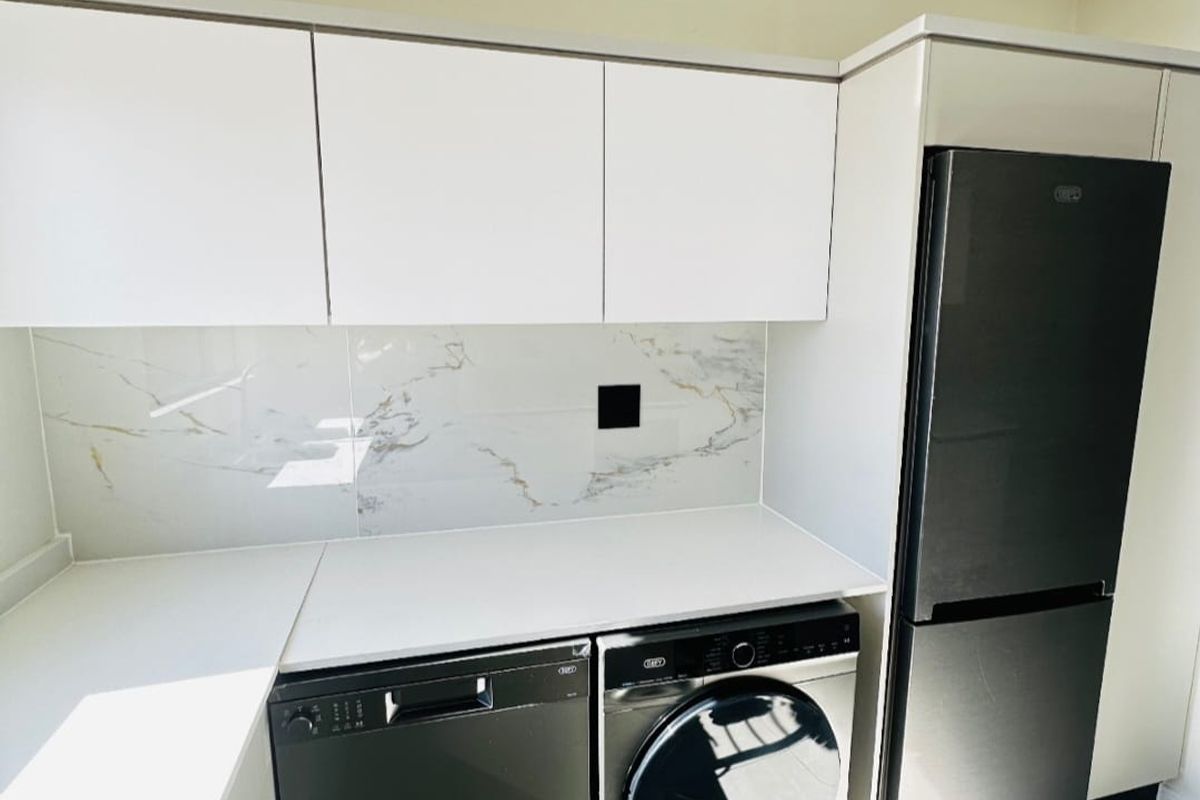 Modern kitchen featuring sleek white cabinetry, a marble-look splashback, stone-look countertops, and tiled flooring, presenting a clean and contemporary aesthetic.