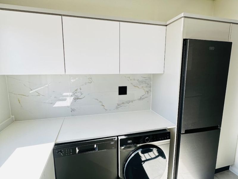 Modern kitchen featuring sleek white cabinetry, a marble-look splashback, stone-look countertops, and tiled flooring, presenting a clean and contemporary aesthetic.
