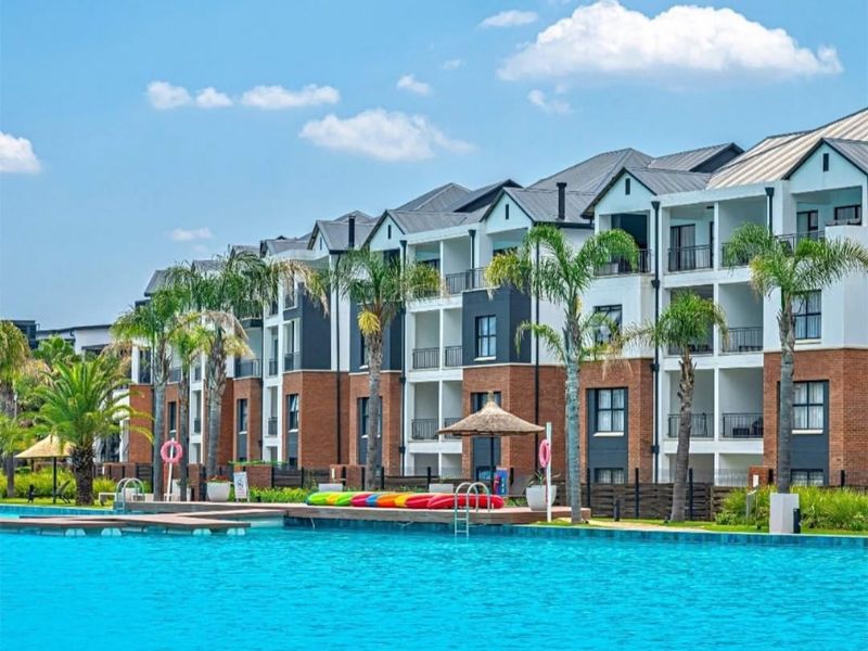 A well-maintained apartment complex featuring a large swimming pool, landscaped grounds, and private balconies with modern brick and render finishes.