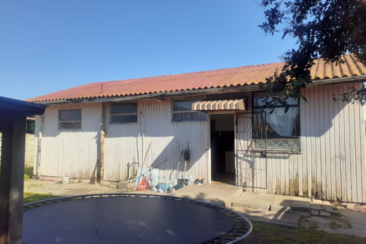 Rear view of a detached house featuring timber cladding, a corrugated metal roof, and a security-gated entrance with concrete steps.