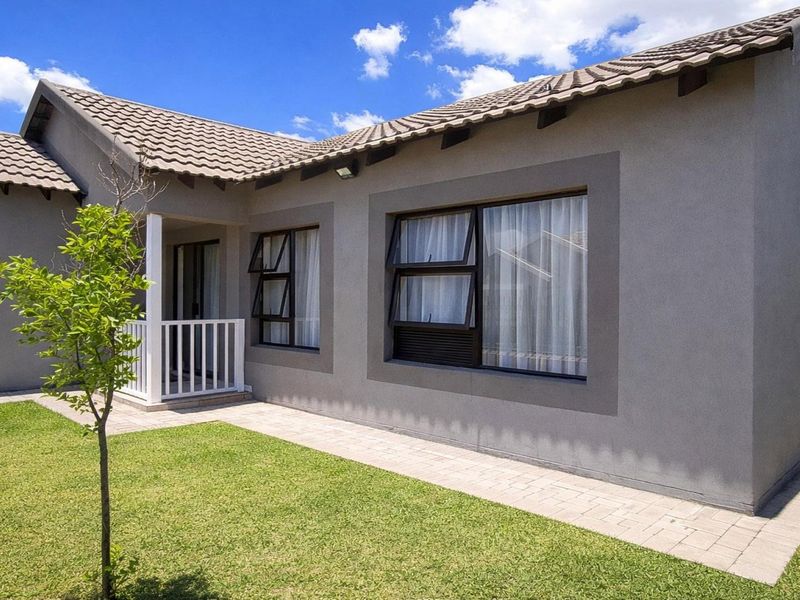 A well-maintained rear exterior view of the house featuring a paved walkway, a small covered patio area, and a neat lawn.