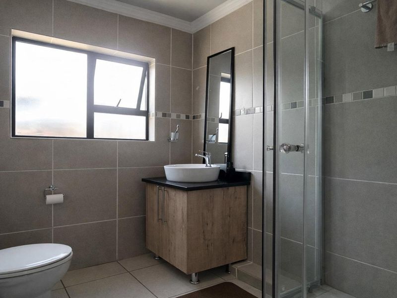 Modern bathroom featuring a vanity cabinet with vessel sink, glass shower enclosure, and neutral floor-to-ceiling wall tiling.