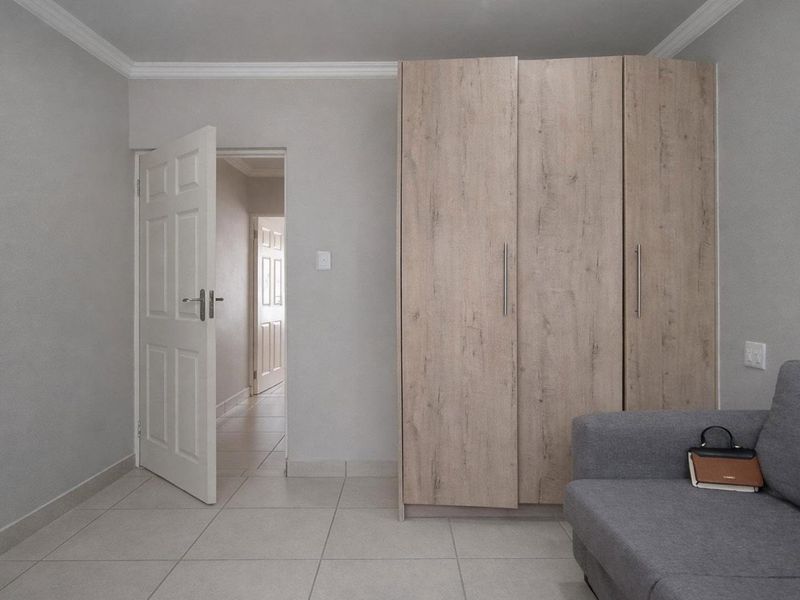A clean bedroom featuring neutral tiled flooring, a modern built-in wardrobe with wood-grain finish, and classic panel doors leading to the hallway.