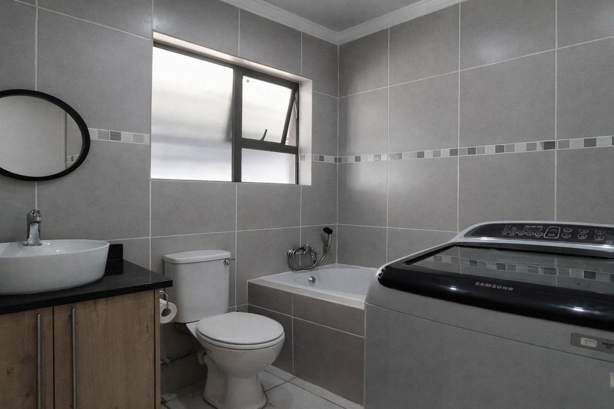 A modern bathroom featuring grey wall tiles, a vanity with a vessel sink, a toilet, and a built-in bathtub.