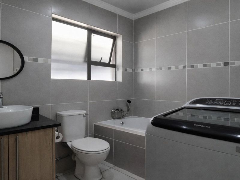 A modern bathroom featuring grey wall tiles, a vanity with a vessel sink, a toilet, and a built-in bathtub.