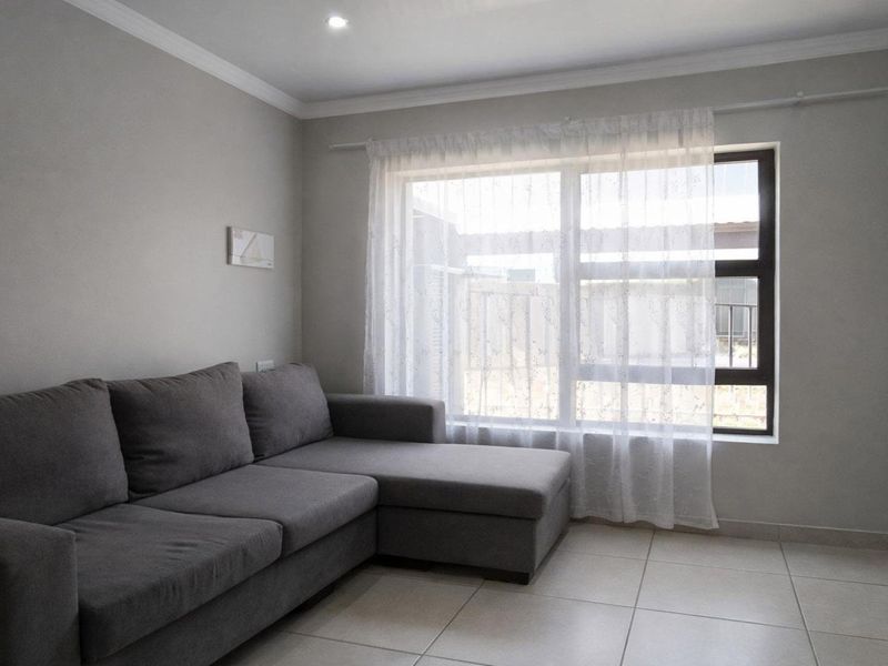 A bright and neutral living room featuring tiled flooring, recessed downlighting, and a large aluminium-framed window.
