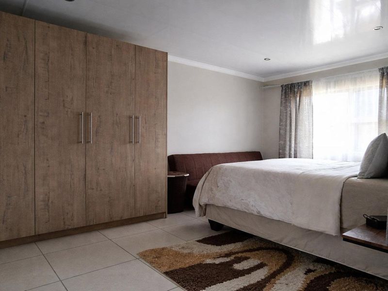 A well-maintained bedroom featuring neutral tiled flooring, recessed ceiling lighting, and extensive built-in wooden cupboards for ample storage.