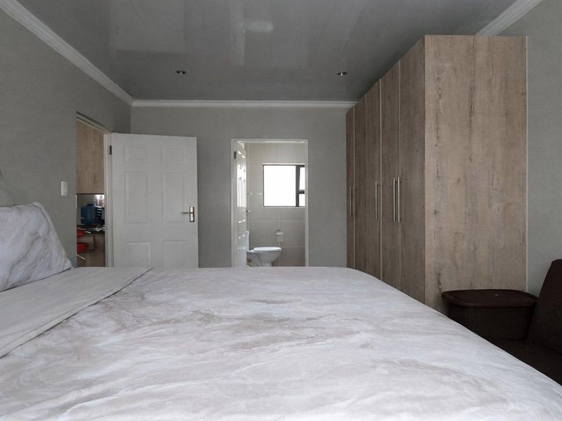 A well-maintained bedroom featuring built-in wooden cupboards, recessed ceiling lighting, and direct access to an en-suite bathroom.