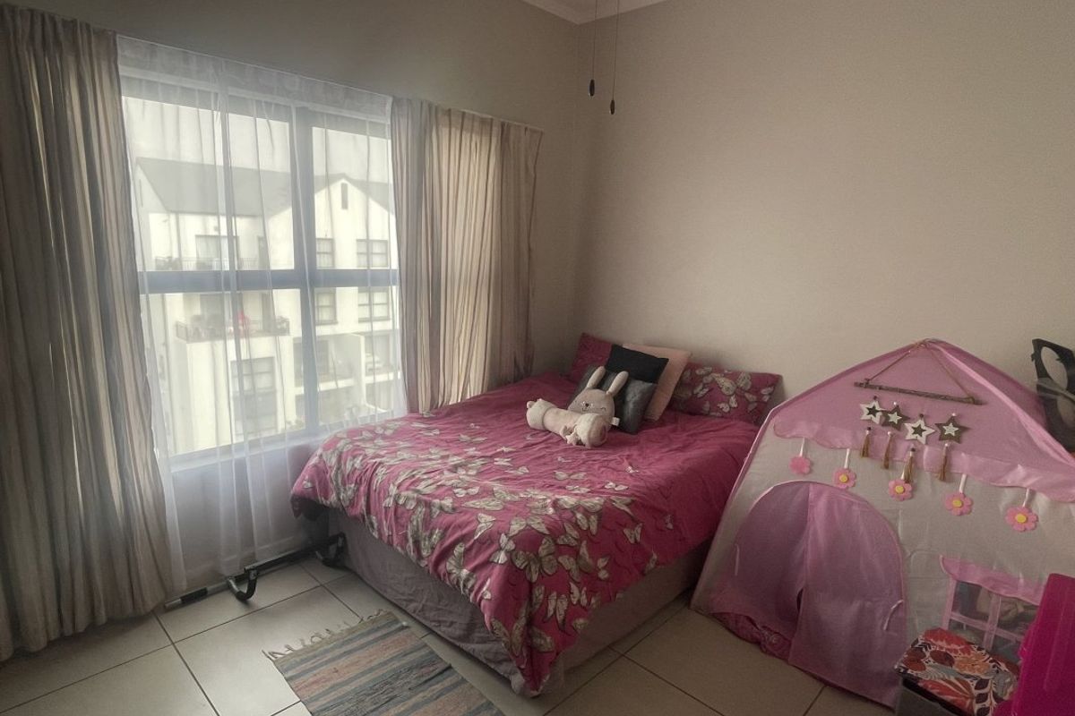 A bedroom featuring tiled flooring and a large window providing natural light, suitable for a child's room or guest bedroom.