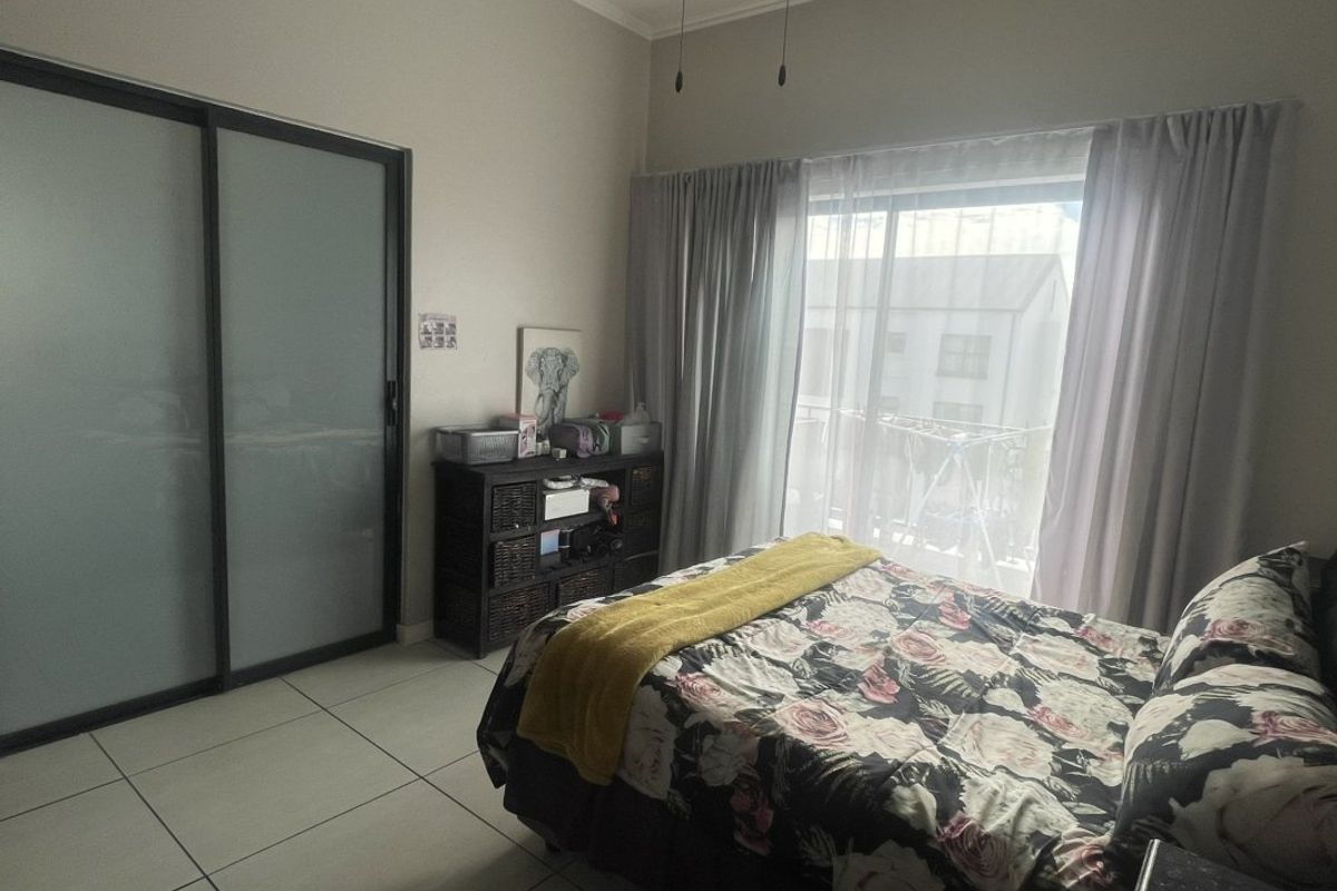 A well-lit bedroom featuring tiled flooring, a modern sliding door wardrobe, and direct access to a balcony through large sliding glass doors.