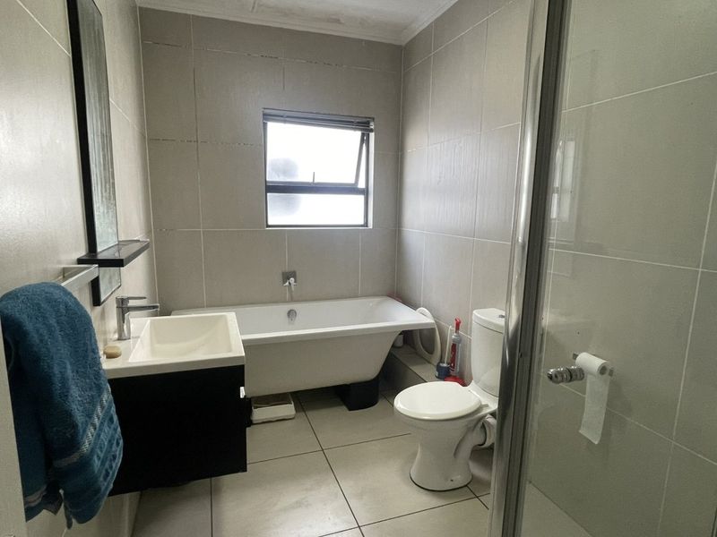 A functional bathroom featuring a freestanding bathtub, wall-mounted basin, toilet, and a glass-enclosed shower with neutral floor-to-ceiling tiling.