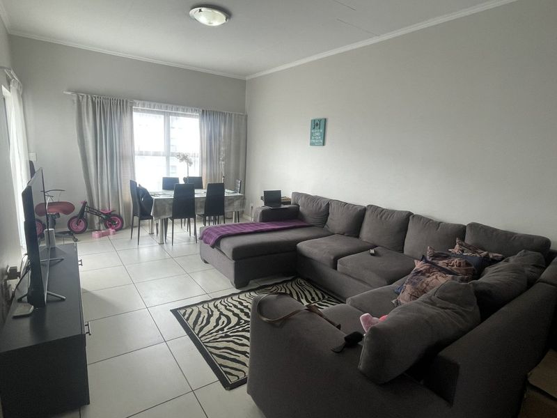 An open-plan living and dining area featuring neutral tiled flooring, a large window for natural light, and a functional layout.