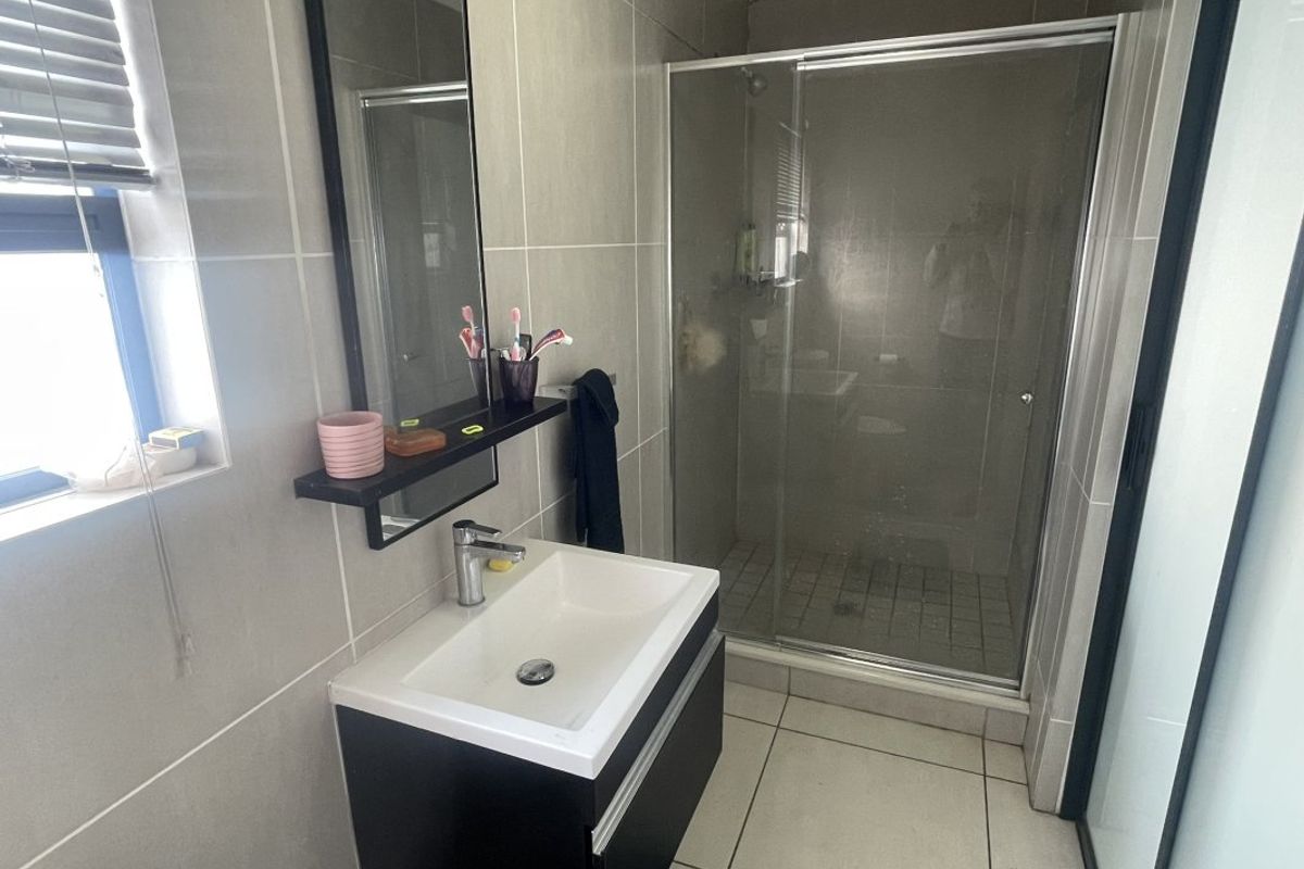 A modern bathroom featuring a vanity basin, a glass-enclosed shower, and neutral wall and floor tiling.