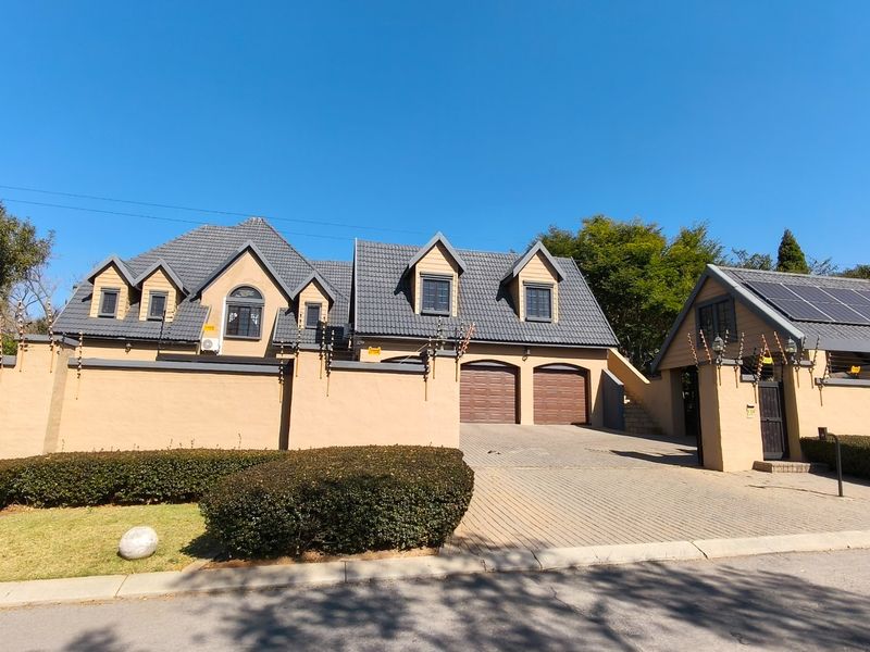 Front elevation of a well-maintained house featuring a tiled roof, double garage, paved driveway, and secure perimeter wall with electric fencing.