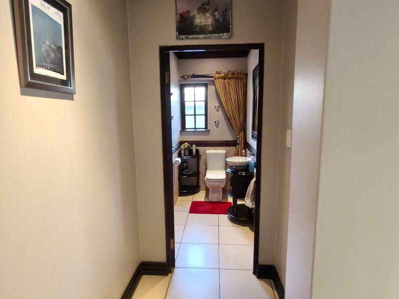 A compact guest bathroom featuring a toilet, vessel sink, and tiled flooring, viewed from the adjacent hallway.