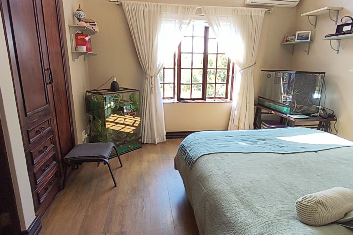 A well-maintained bedroom featuring laminate flooring, a large built-in wooden wardrobe, wall-mounted shelving, and an air conditioning unit.