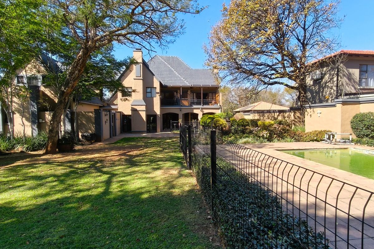 Rear view of the property featuring a swimming pool, paved surround, wire fencing, and a multi-story building with a balcony and tiled roof.