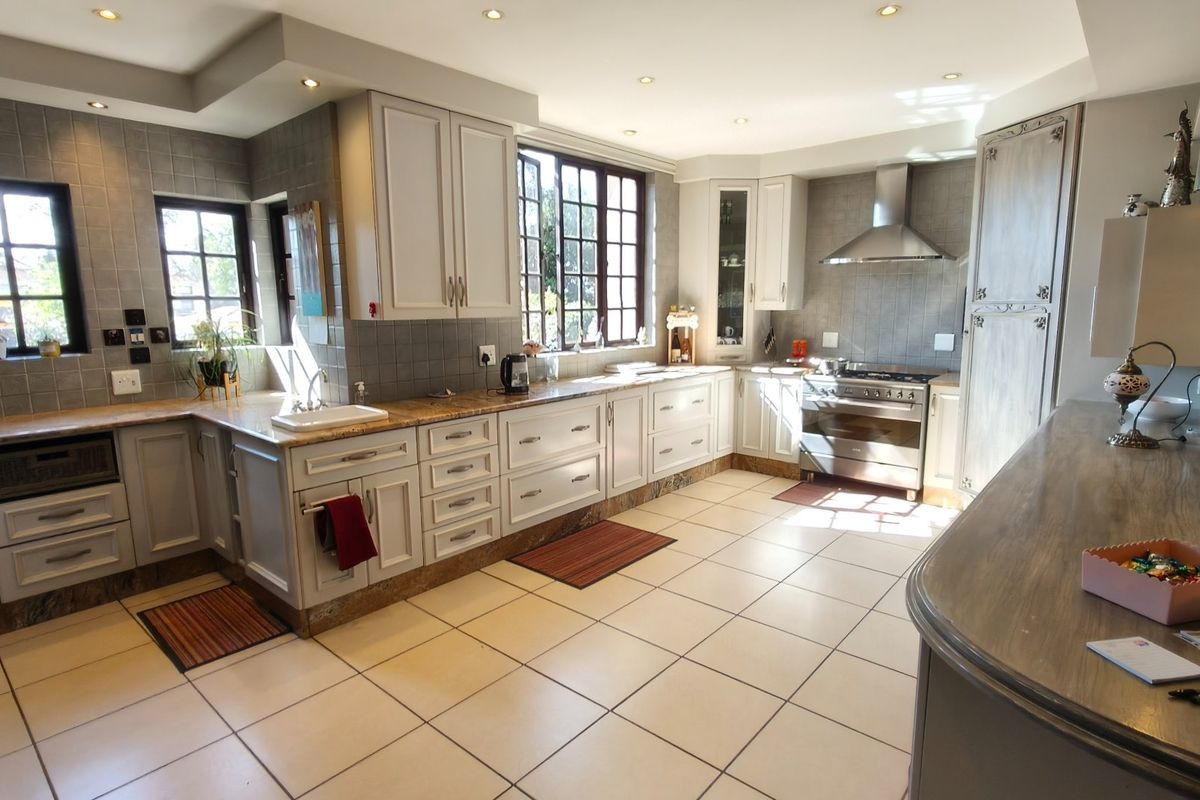 Spacious kitchen featuring light-toned cabinetry, stone countertops, stainless steel gas stove with extractor fan, and neutral ceramic tile flooring.