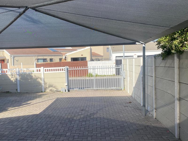 A paved driveway area featuring a shade sail, enclosed by perimeter walls and a secure metal gate.