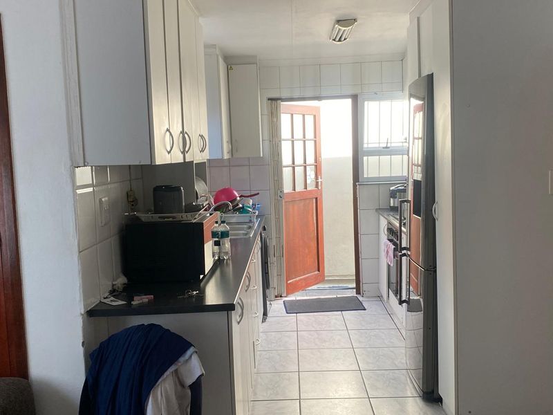A functional galley-style kitchen featuring white built-in cabinetry, tiled flooring, and direct access to an outdoor area.