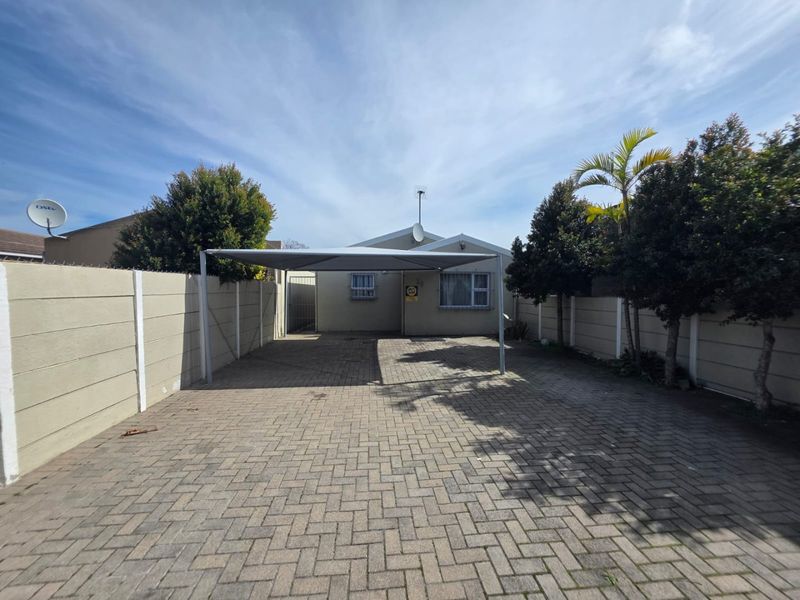 Front exterior view featuring a paved driveway, a shade sail carport, and secure precast concrete boundary walls.