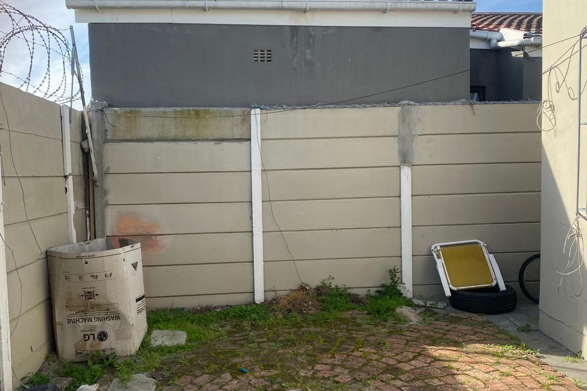 A rear courtyard area featuring a precast concrete boundary wall with security razor wire and paved flooring requiring maintenance.