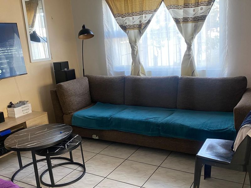 A living room area featuring tiled flooring and a window fitted with security bars, providing natural light to the space.
