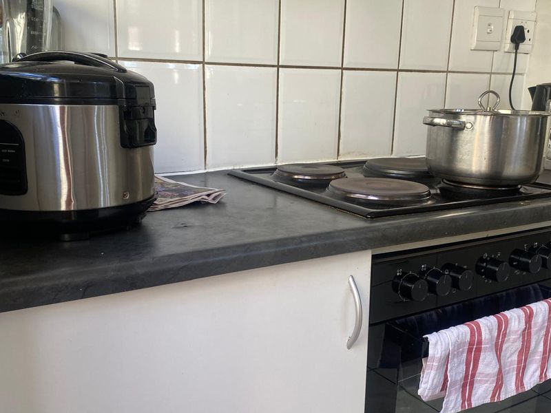 A functional kitchen area featuring a built-in electric oven, hob, and white tiled splashback with dark laminate countertops.