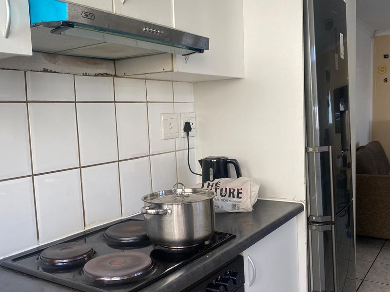 A compact kitchen area featuring a built-in electric hob, stainless steel extractor fan, and tiled backsplash with white cabinetry.