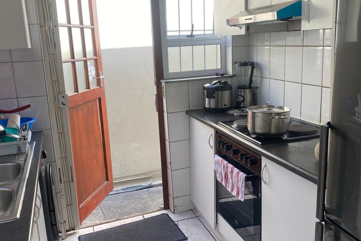 Compact kitchen featuring built-in cabinetry, electric stove with extractor fan, double sink, and direct access to an outdoor area.