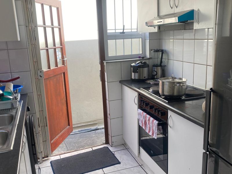 Compact kitchen featuring built-in cabinetry, electric stove with extractor fan, double sink, and direct access to an outdoor area.